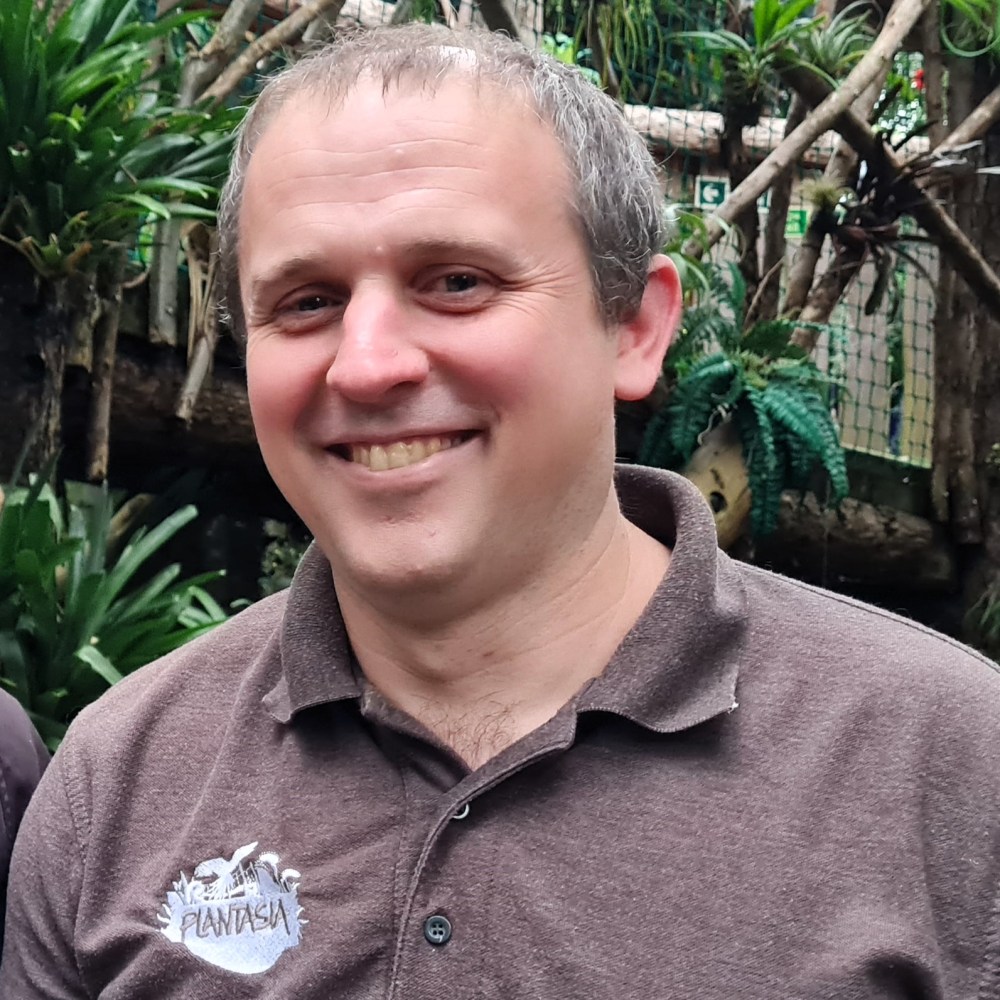 a smiling man standing amongst large green plants